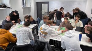 Eine Gruppe an jungen Menschen sitzt an Tischen.